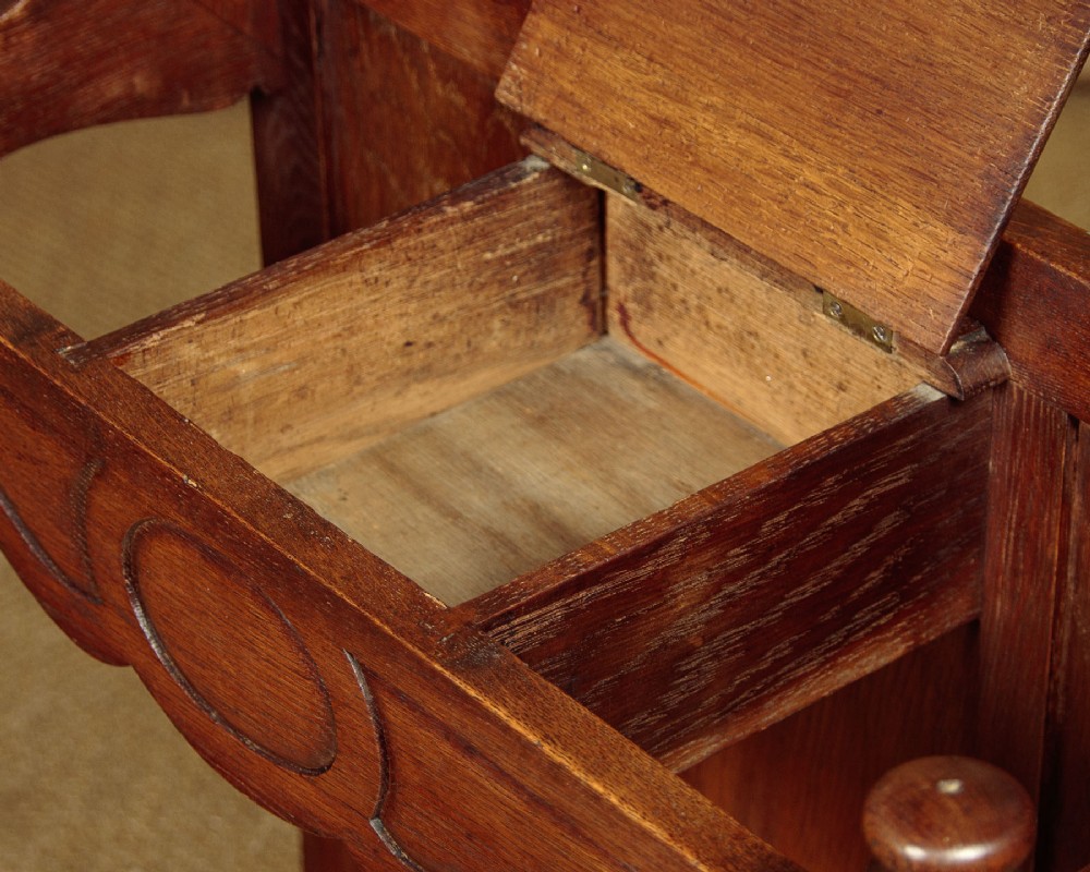An Art Nouveau oak hallstand featuring an arched upper frame, brass coat hooks, central mirror, glove box, and bottom umbrella stand with two brass drip trays. View VIII