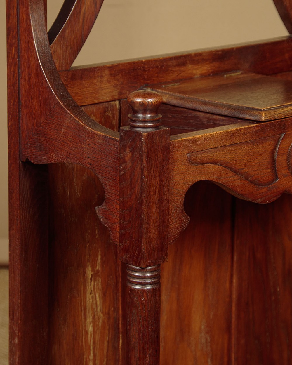 An Art Nouveau oak hallstand featuring an arched upper frame, brass coat hooks, central mirror, glove box, and bottom umbrella stand with two brass drip trays. View IX