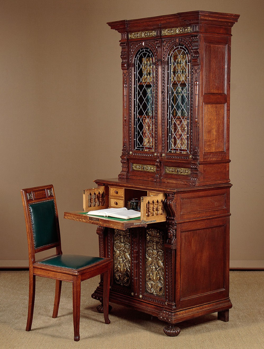 A carved dark oak Victorian secretaire bookcase featuring leaded glass upper doors, embossed brass panels, and gadrooned feet. View II