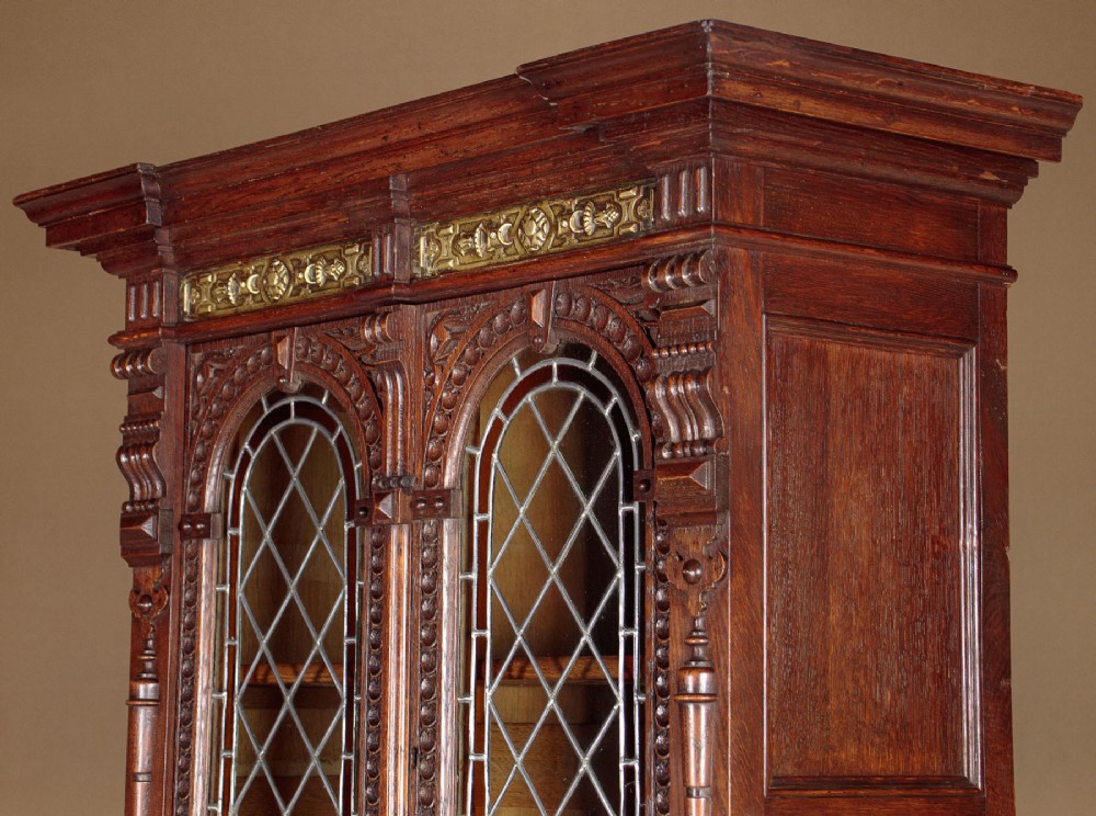 A carved dark oak Victorian secretaire bookcase featuring leaded glass upper doors, embossed brass panels, and gadrooned feet. View IV