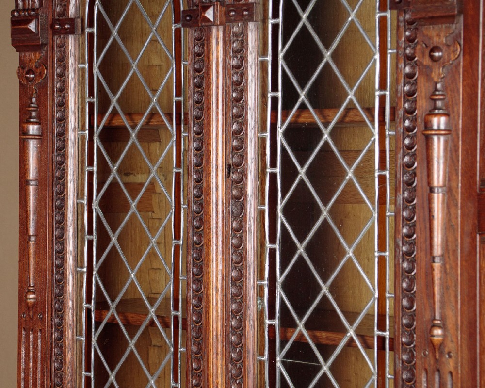 A carved dark oak Victorian secretaire bookcase featuring leaded glass upper doors, embossed brass panels, and gadrooned feet. View V