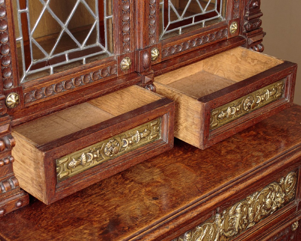 A carved dark oak Victorian secretaire bookcase featuring leaded glass upper doors, embossed brass panels, and gadrooned feet. View VII