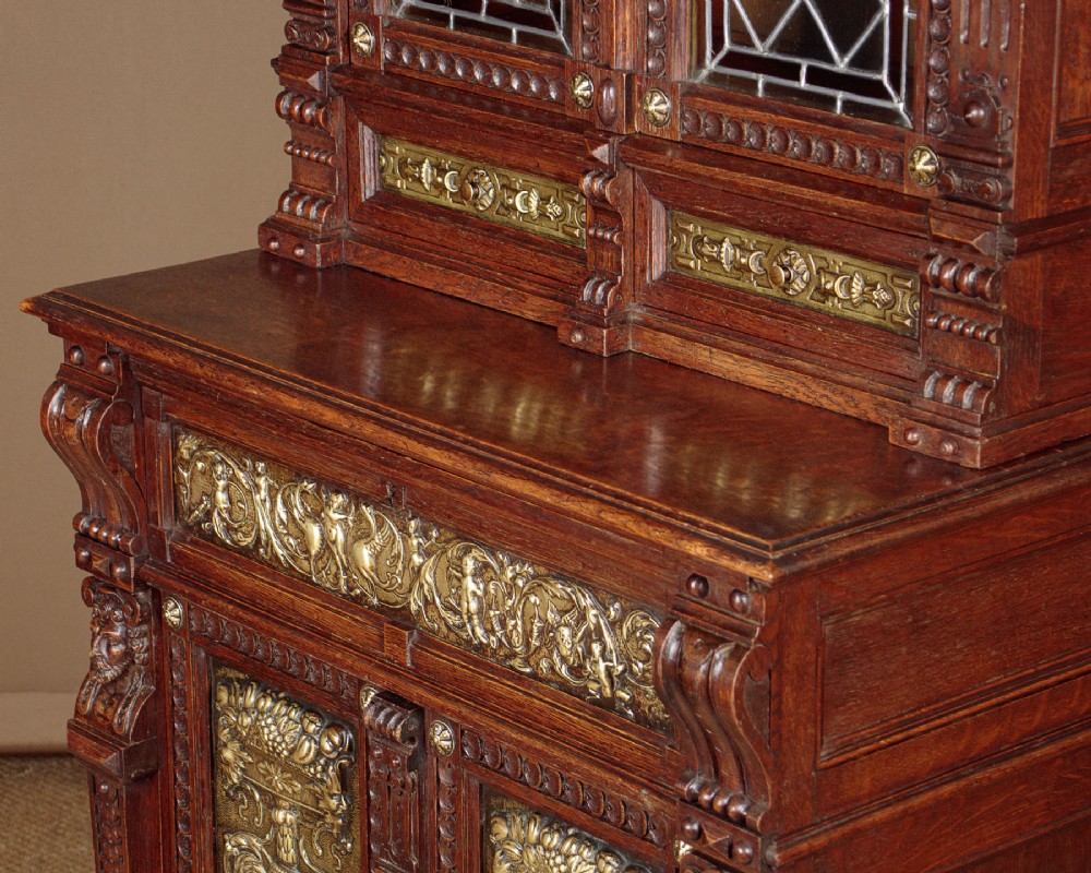 A carved dark oak Victorian secretaire bookcase featuring leaded glass upper doors, embossed brass panels, and gadrooned feet. View VIII