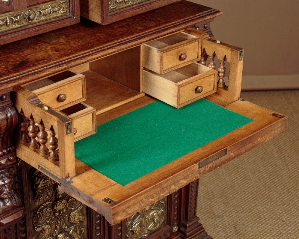 A carved dark oak Victorian secretaire bookcase featuring leaded glass upper doors, embossed brass panels, and gadrooned feet. View IX