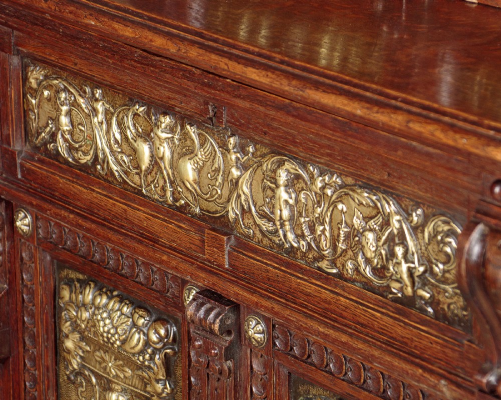 A carved dark oak Victorian secretaire bookcase featuring leaded glass upper doors, embossed brass panels, and gadrooned feet. View X