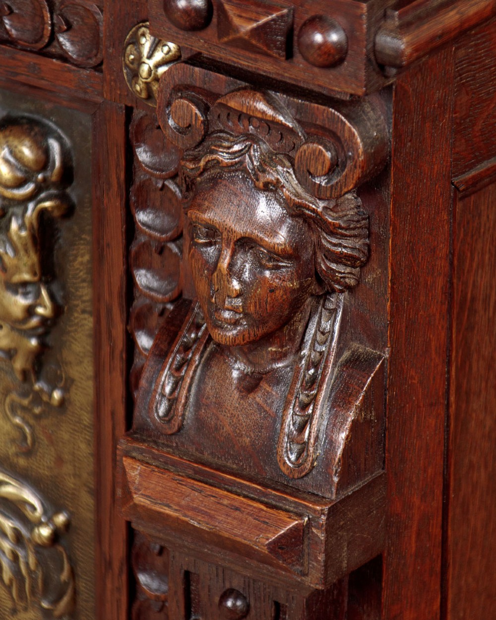 A carved dark oak Victorian secretaire bookcase featuring leaded glass upper doors, embossed brass panels, and gadrooned feet. View XII