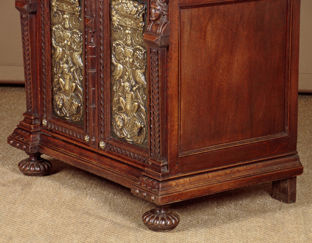 A carved dark oak Victorian secretaire bookcase featuring leaded glass upper doors, embossed brass panels, and gadrooned feet. View XIII