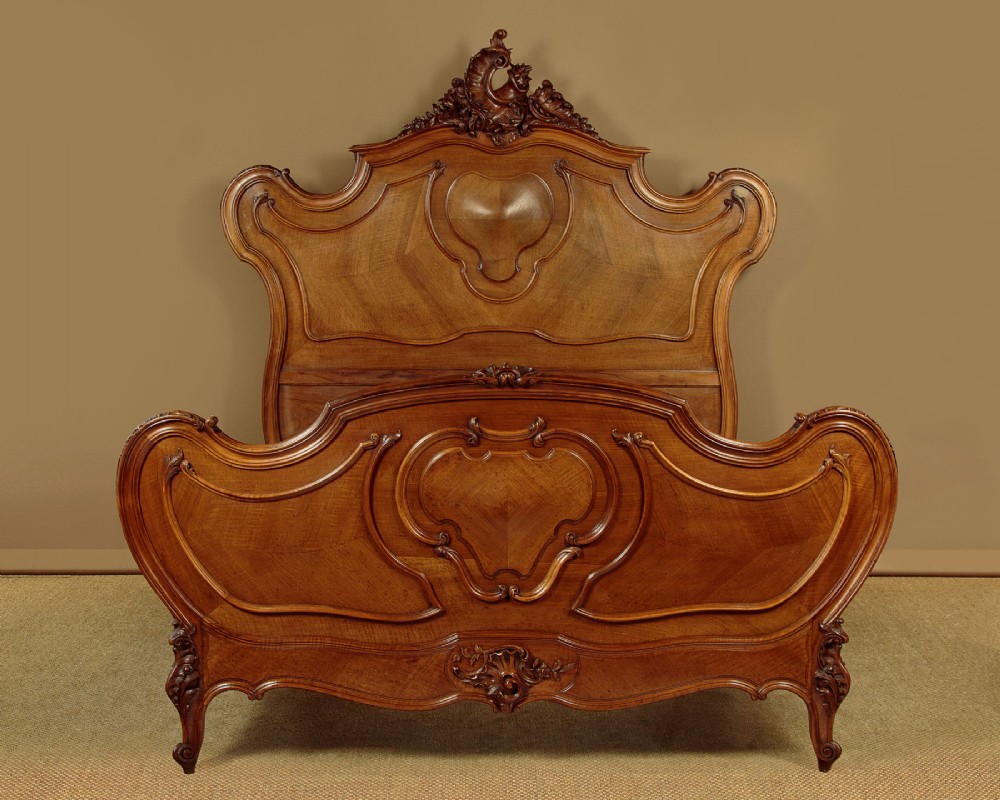 An antique French double bed frame crafted from carved walnut featuring serpentine edges, shell motifs, and book-matched veneered panels on the headboard and footboard.