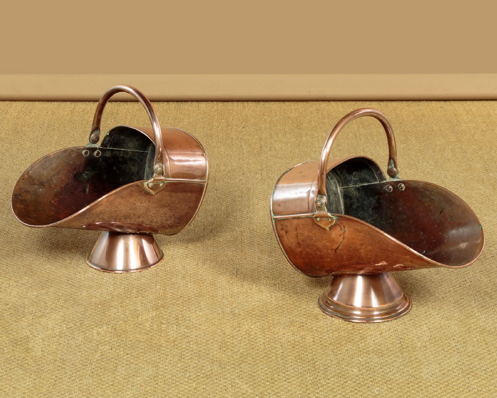 A pair of Victorian copper helmet-style coal scuttles featuring flared circular pedestals and curved swing handles. View II