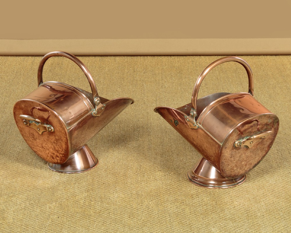 A pair of Victorian copper helmet-style coal scuttles featuring flared circular pedestals and curved swing handles. View III