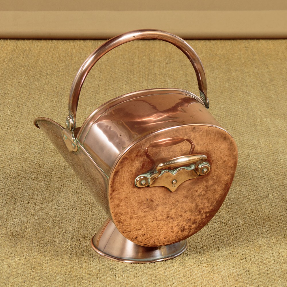 A pair of Victorian copper helmet-style coal scuttles featuring flared circular pedestals and curved swing handles. View V