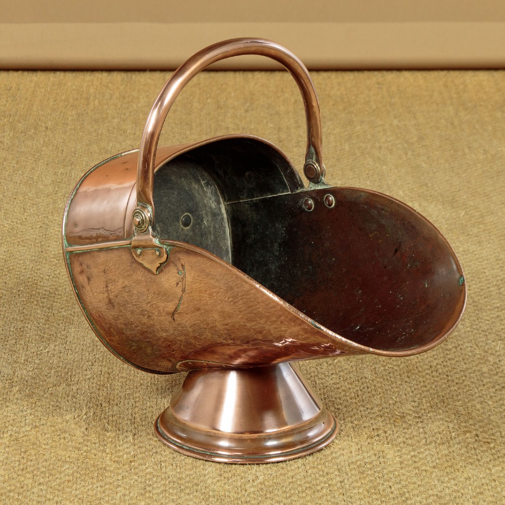 A pair of Victorian copper helmet-style coal scuttles featuring flared circular pedestals and curved swing handles. View VI