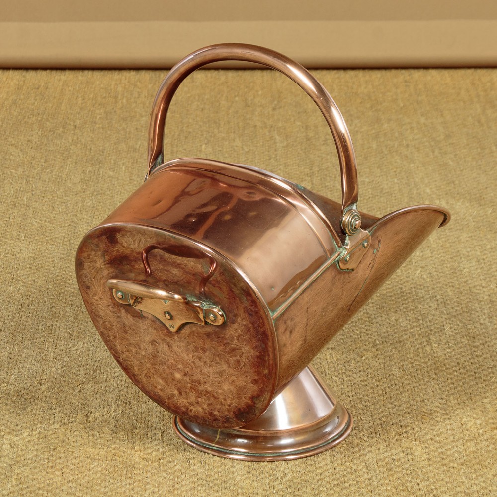 A pair of Victorian copper helmet-style coal scuttles featuring flared circular pedestals and curved swing handles. View VII