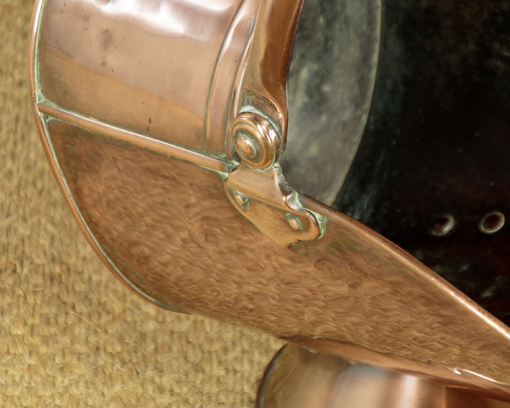 A pair of Victorian copper helmet-style coal scuttles featuring flared circular pedestals and curved swing handles. View X