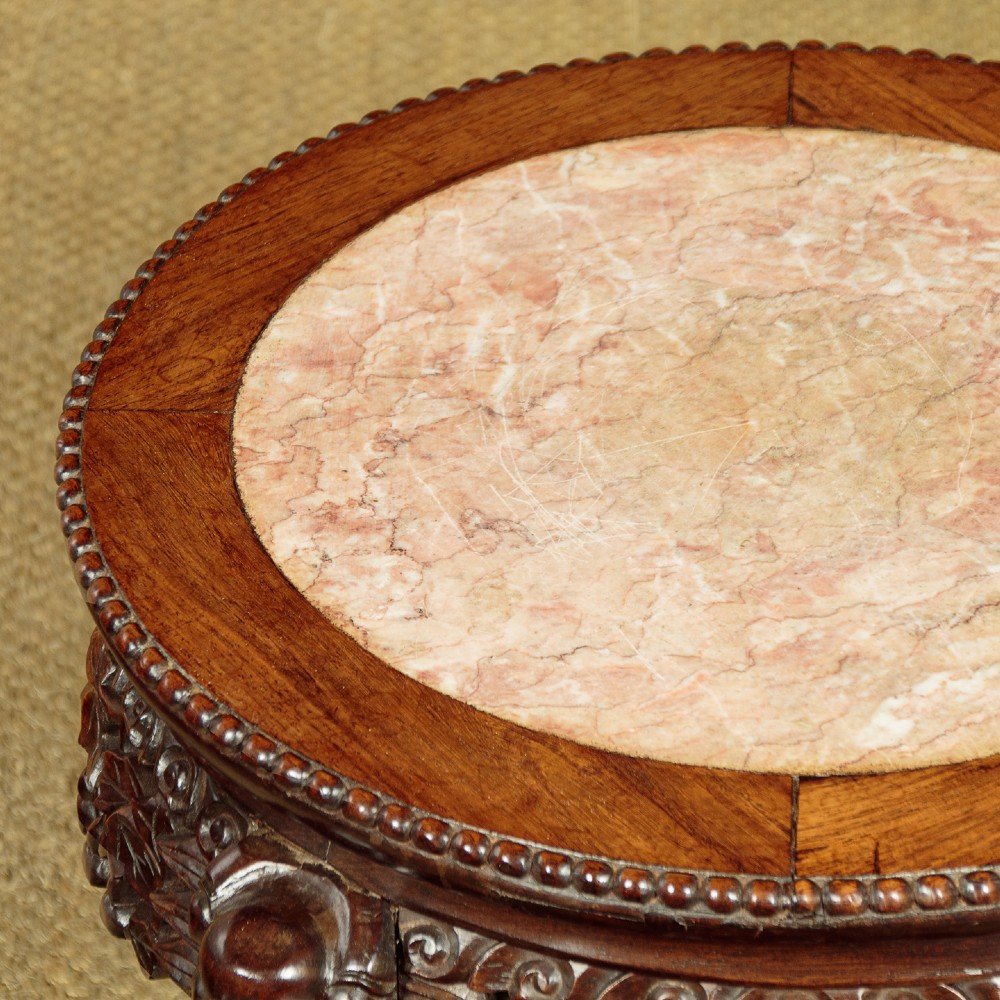 A low circular dark hardwood side table featuring an inset circular pink marble top, deeply carved floral aprons, and cabriole legs terminating in claw feet. View V