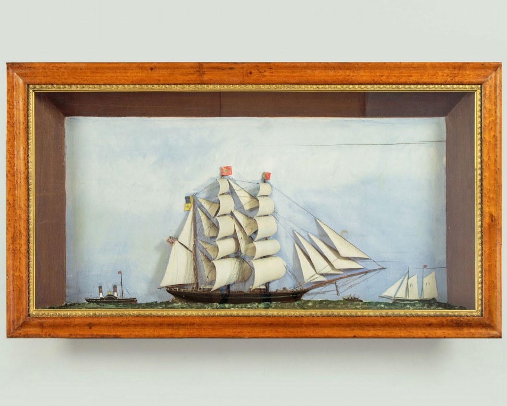 A three-dimensional antique maritime diorama featuring a three-masted sailing ship framed in a deep glazed wooden box with a painted sky and sea background.