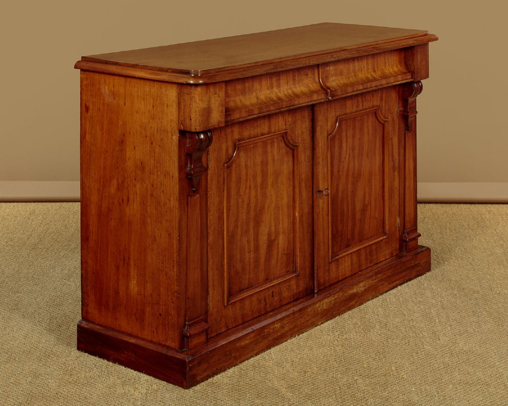 A mid-19th-century Victorian mahogany sideboard featuring a smooth flat top, two frieze drawers, and a pair of panelled cupboard doors flanked by carved corbels. View II
