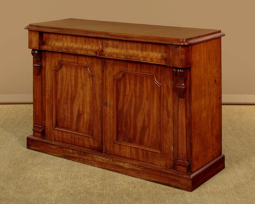 A mid-19th-century Victorian mahogany sideboard featuring a smooth flat top, two frieze drawers, and a pair of panelled cupboard doors flanked by carved corbels. View III