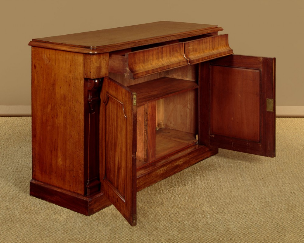 A mid-19th-century Victorian mahogany sideboard featuring a smooth flat top, two frieze drawers, and a pair of panelled cupboard doors flanked by carved corbels. View IV