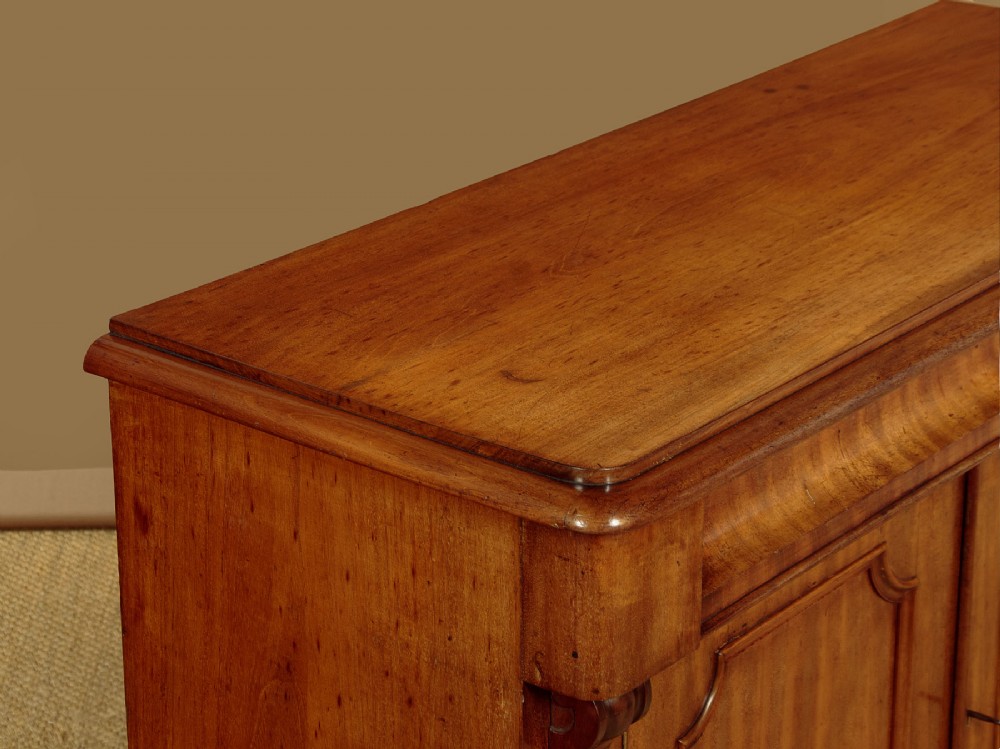 A mid-19th-century Victorian mahogany sideboard featuring a smooth flat top, two frieze drawers, and a pair of panelled cupboard doors flanked by carved corbels. View VI