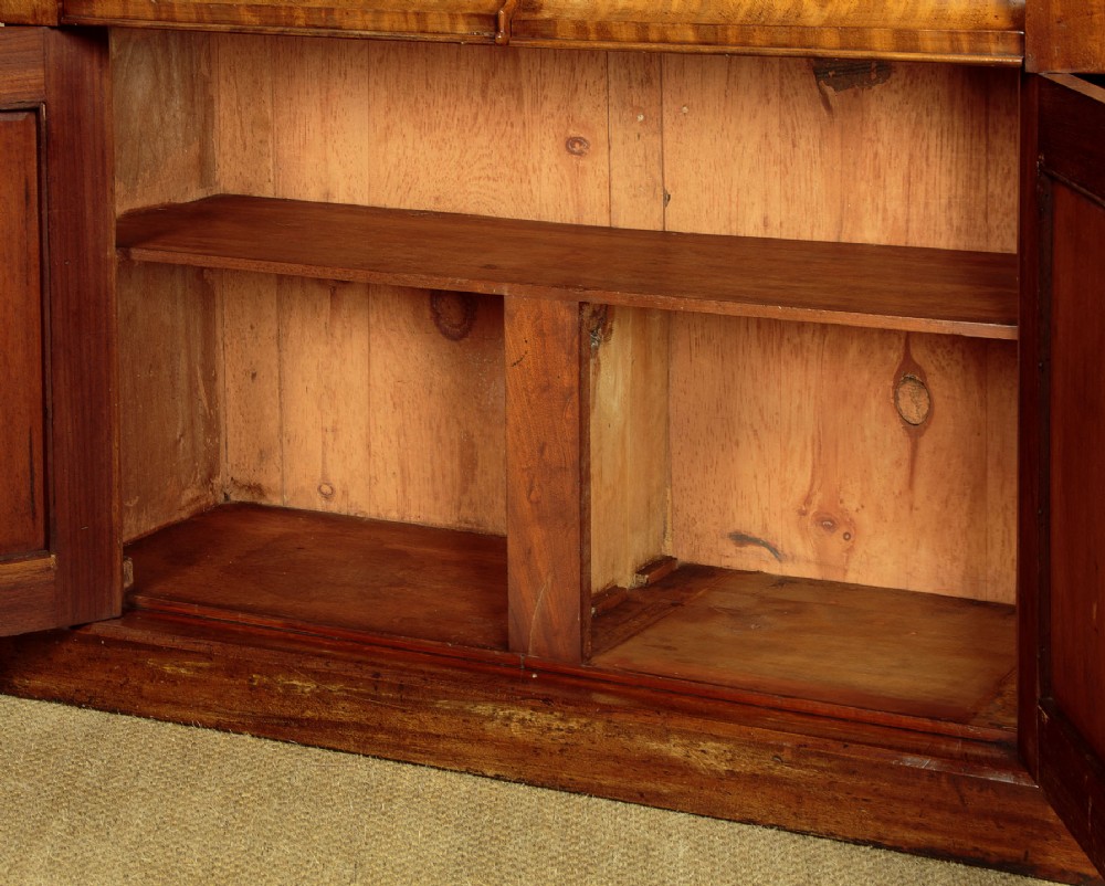 A mid-19th-century Victorian mahogany sideboard featuring a smooth flat top, two frieze drawers, and a pair of panelled cupboard doors flanked by carved corbels. View X