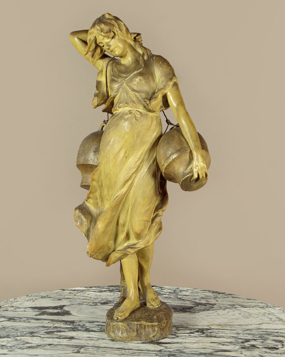 An Art Nouveau terracotta sculpture depicting a draped female water carrier holding two vessels.