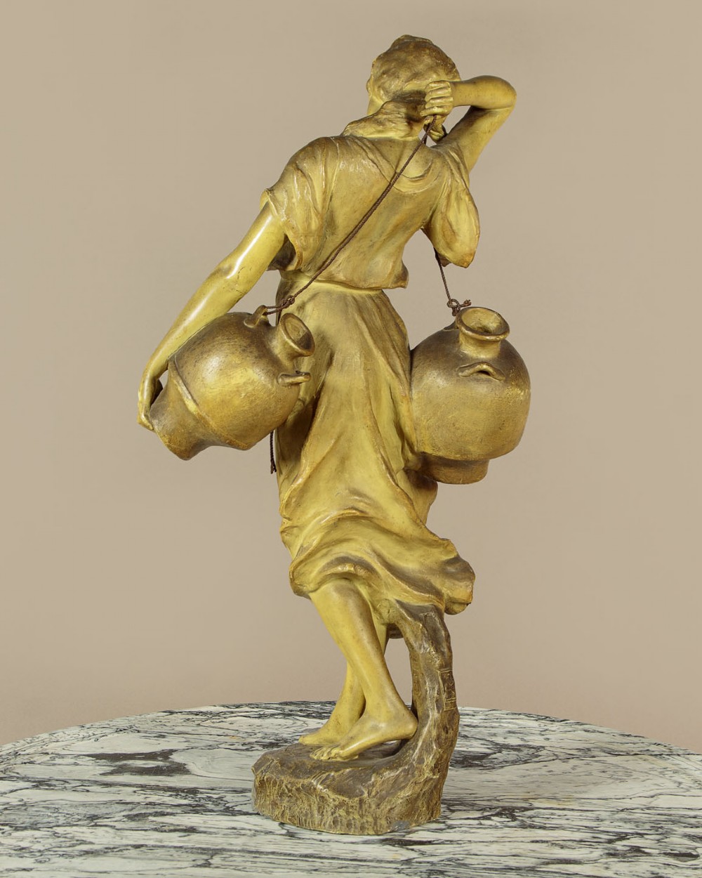 An Art Nouveau terracotta sculpture depicting a draped female water carrier holding two vessels. View IV
