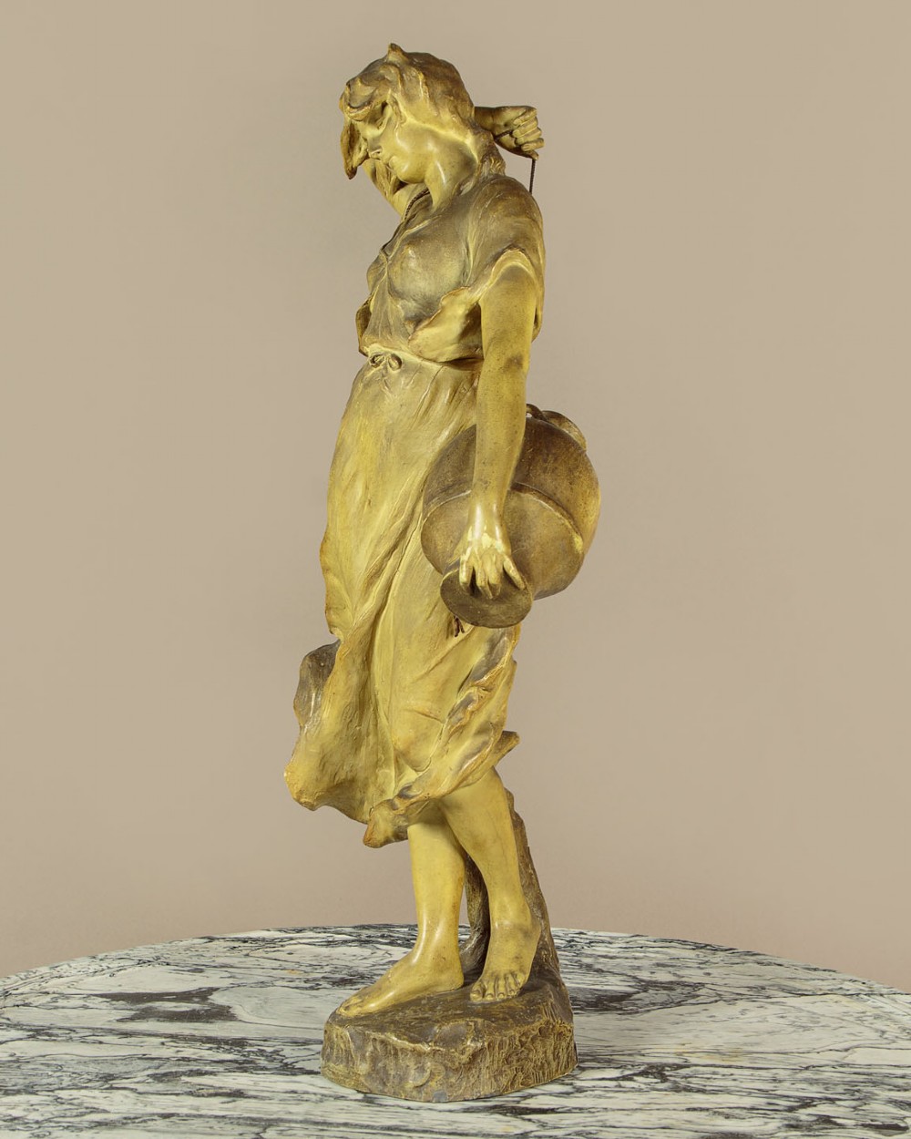 An Art Nouveau terracotta sculpture depicting a draped female water carrier holding two vessels. View V