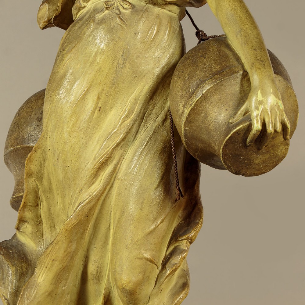 An Art Nouveau terracotta sculpture depicting a draped female water carrier holding two vessels. View IX