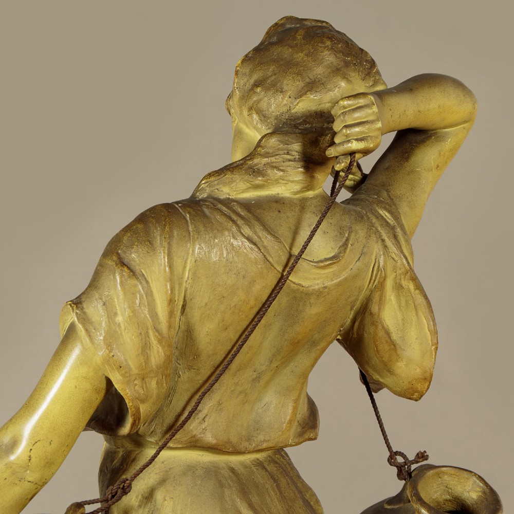 An Art Nouveau terracotta sculpture depicting a draped female water carrier holding two vessels. View X