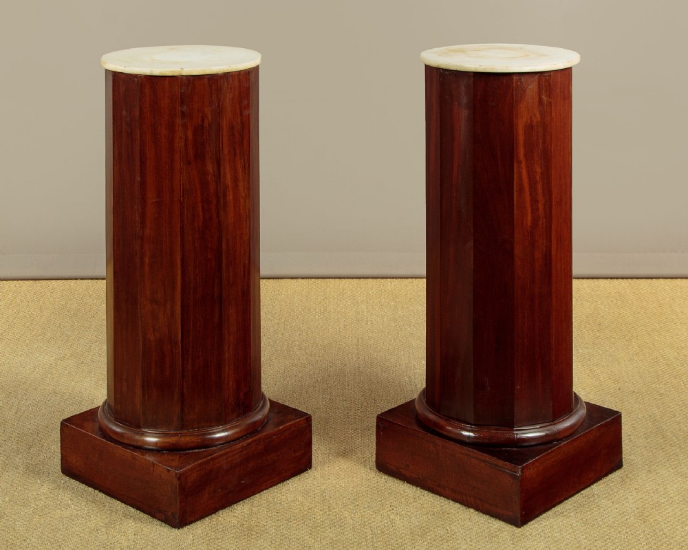 A pair of antique dark mahogany column pedestals featuring circular white marble tops and heavy square plinth bases.