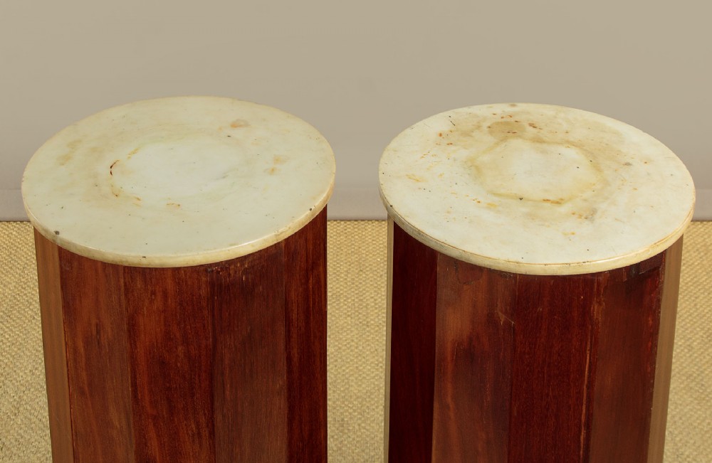 A pair of antique dark mahogany column pedestals featuring circular white marble tops and heavy square plinth bases. View IV