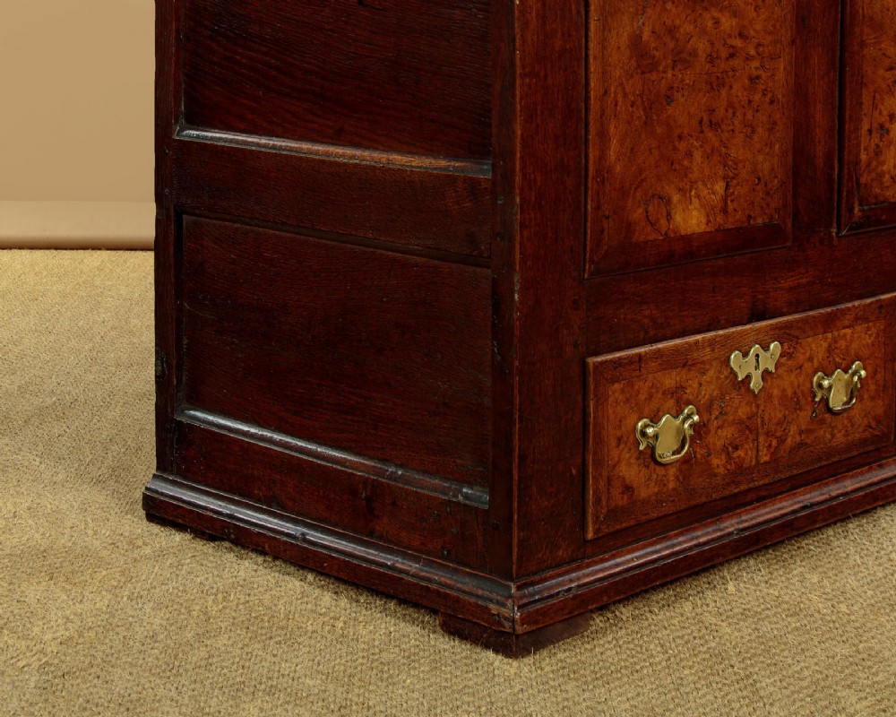 A late eighteenth-century Georgian dark oak mule chest featuring three burr elm inset panels and two lower drawers with brass handles. View X