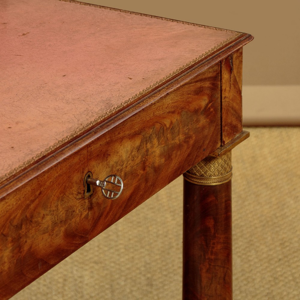 A French Empire flame mahogany dressing table featuring an arched swing mirror flanked by column supports with brass mounts, small trinket drawers, and a pink leather writing surface. View VII