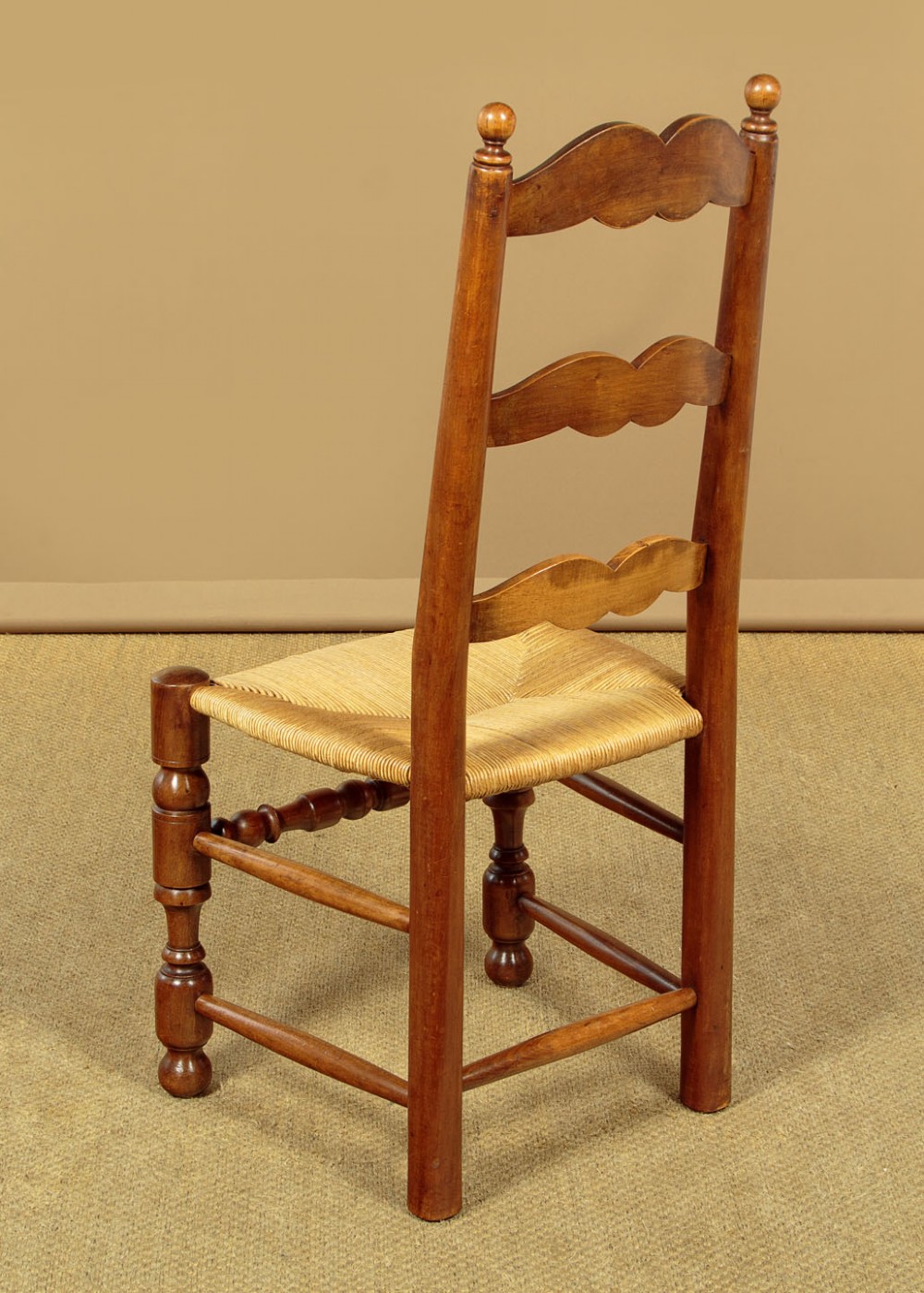 A set of six wooden ladderback dining chairs featuring wavy back slats, turned front legs, and woven rush seats. View X
