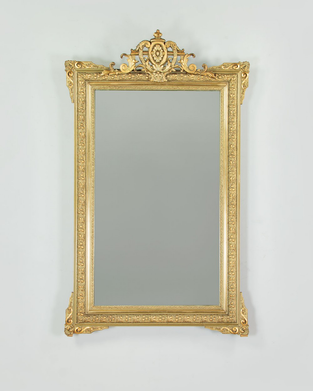 An antique rectangular French wall mirror featuring a gold gilded frame, ornate carved top cresting, and decorative floral mouldings.