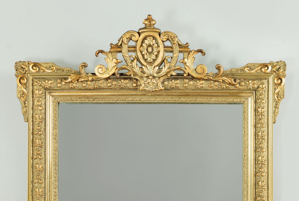 An antique rectangular French wall mirror featuring a gold gilded frame, ornate carved top cresting, and decorative floral mouldings. View IV