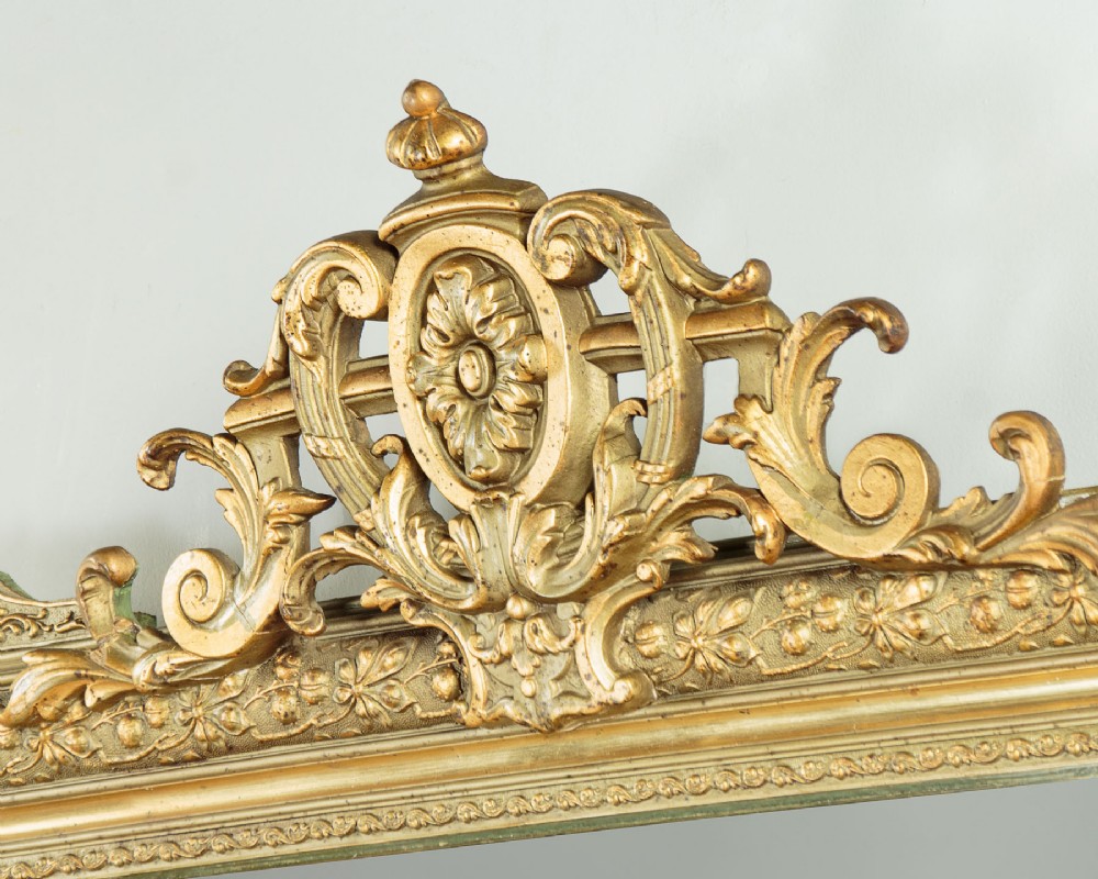 An antique rectangular French wall mirror featuring a gold gilded frame, ornate carved top cresting, and decorative floral mouldings. View V