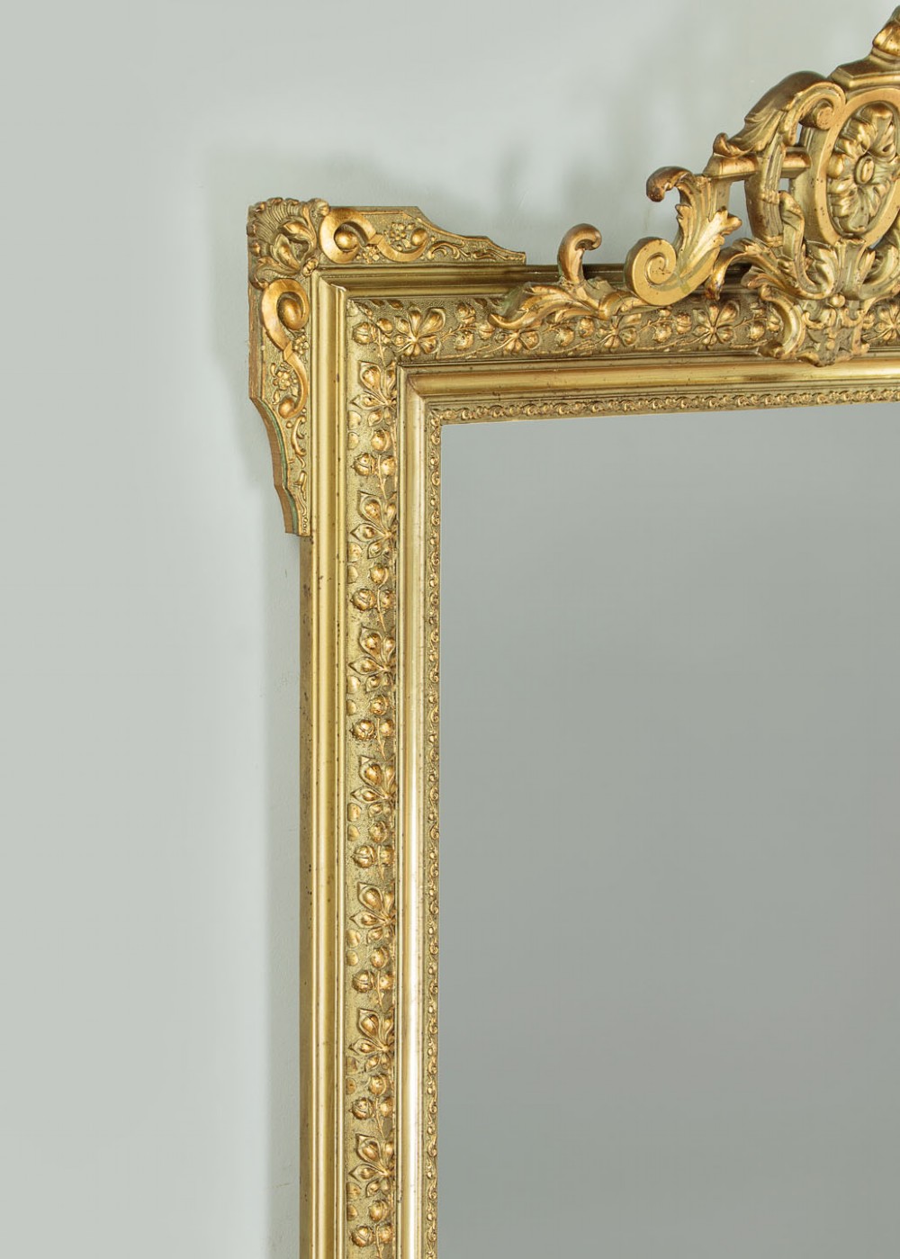 An antique rectangular French wall mirror featuring a gold gilded frame, ornate carved top cresting, and decorative floral mouldings. View VI