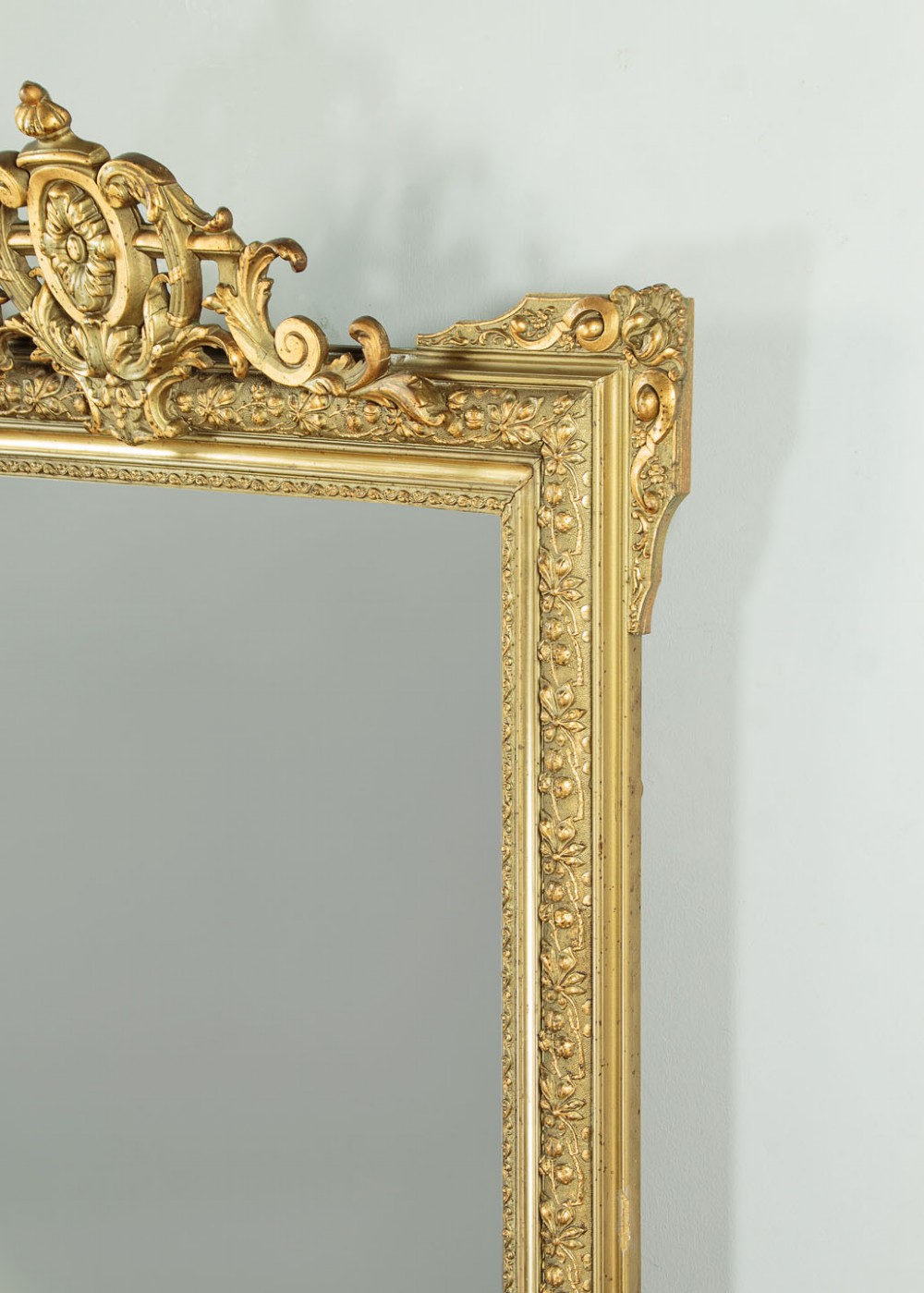 An antique rectangular French wall mirror featuring a gold gilded frame, ornate carved top cresting, and decorative floral mouldings. View VII