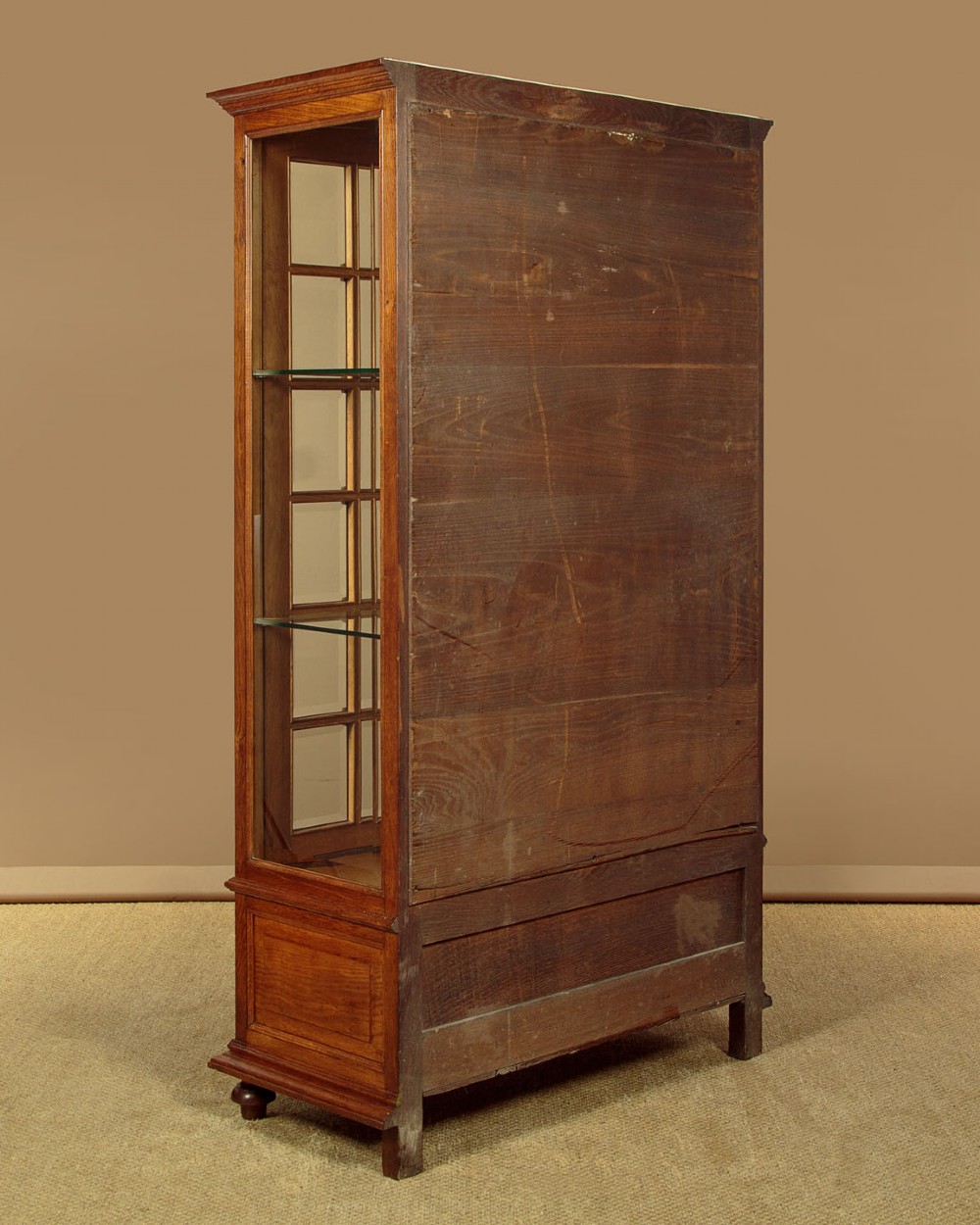 An Edwardian oak display cabinet featuring two glazed doors with gilt rosette mounts, a mirrored interior back, and two drawers at the base with swag handles. View XIII