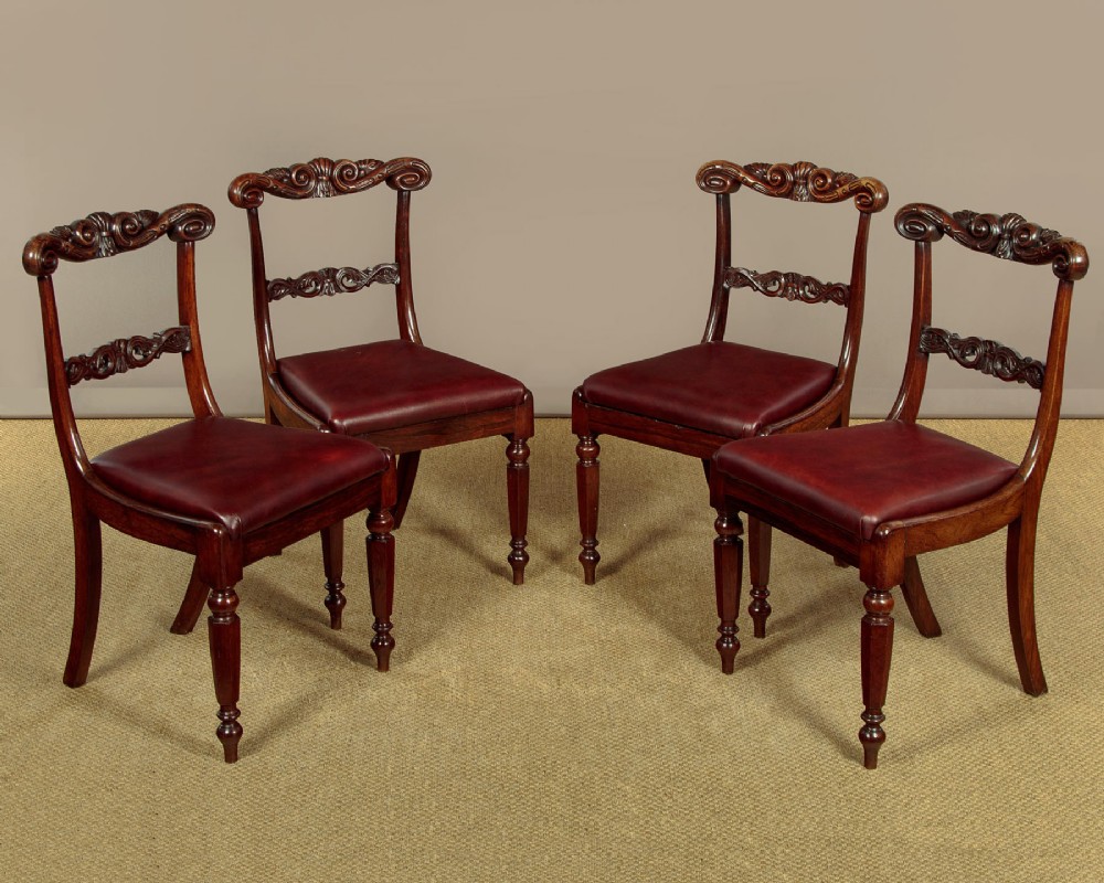 A set of four Regency rosewood dining chairs with carved scroll crest rails, turned front legs, and deep red leather drop-in seats.
