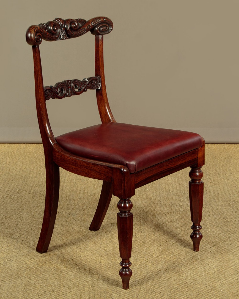 A set of four Regency rosewood dining chairs with carved scroll crest rails, turned front legs, and deep red leather drop-in seats. View II