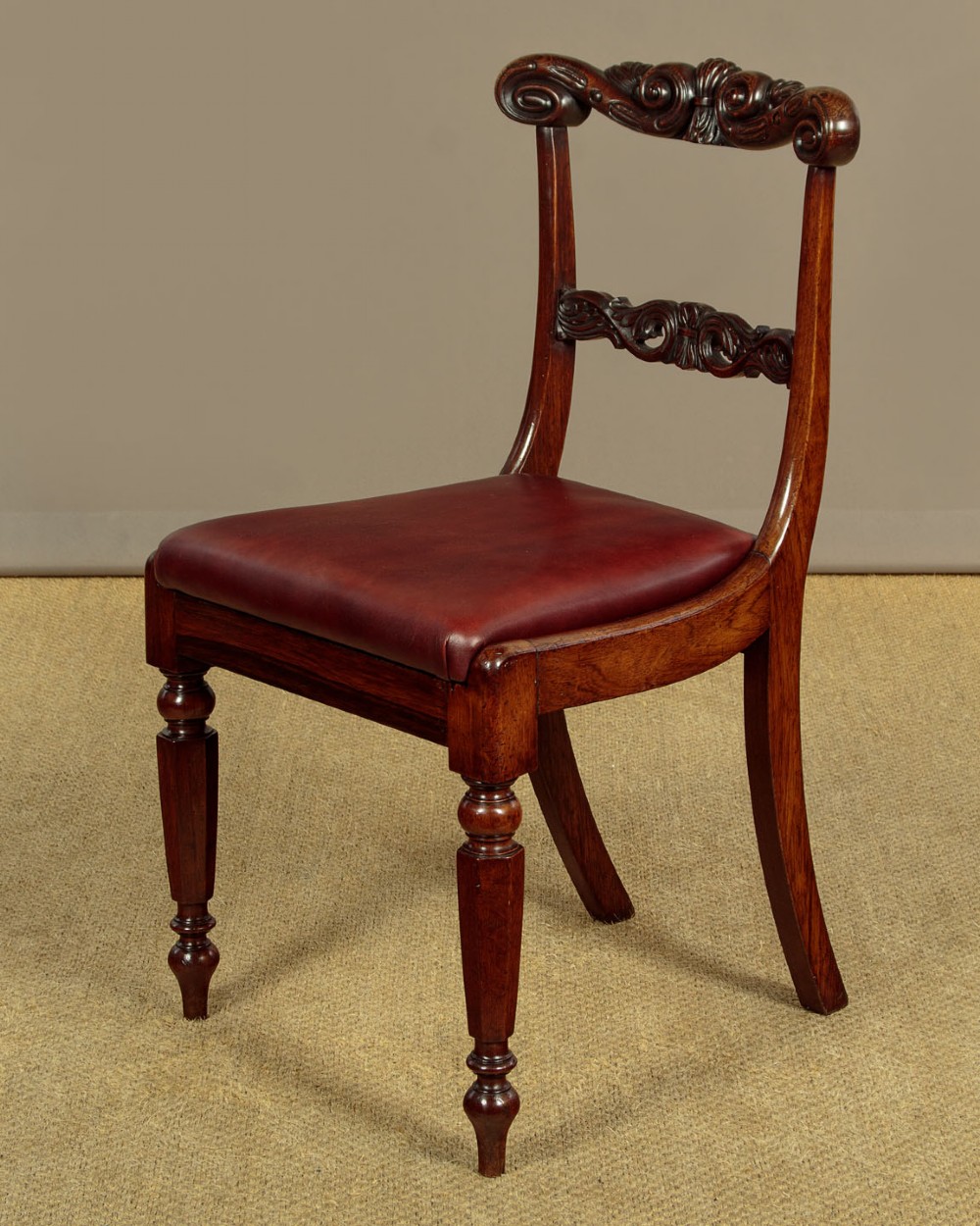 A set of four Regency rosewood dining chairs with carved scroll crest rails, turned front legs, and deep red leather drop-in seats. View IV