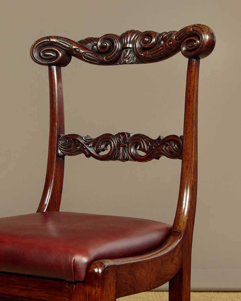 A set of four Regency rosewood dining chairs with carved scroll crest rails, turned front legs, and deep red leather drop-in seats. View V