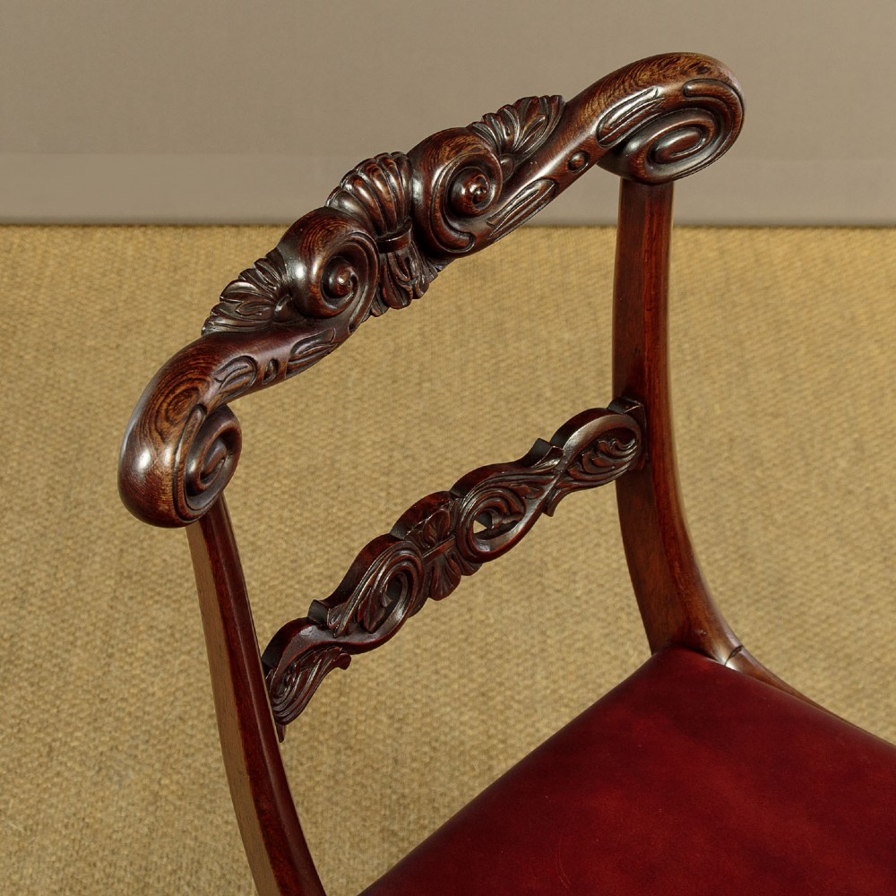 A set of four Regency rosewood dining chairs with carved scroll crest rails, turned front legs, and deep red leather drop-in seats. View VI