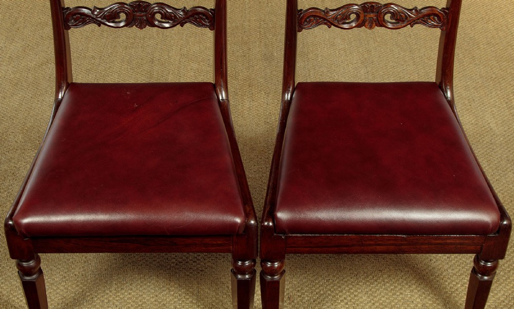 A set of four Regency rosewood dining chairs with carved scroll crest rails, turned front legs, and deep red leather drop-in seats. View IX
