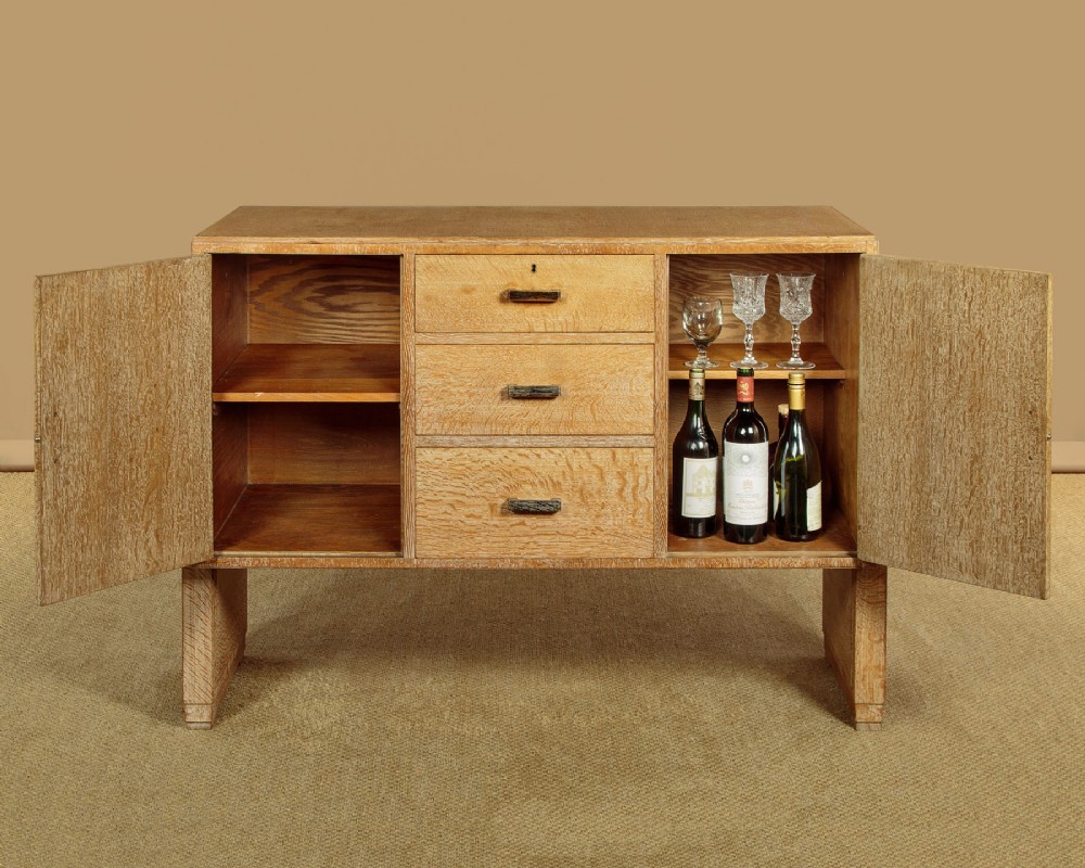 A 1920s limed oak sideboard featuring a central bank of three drawers flanked by two panelled cupboard doors on slab feet. View IV