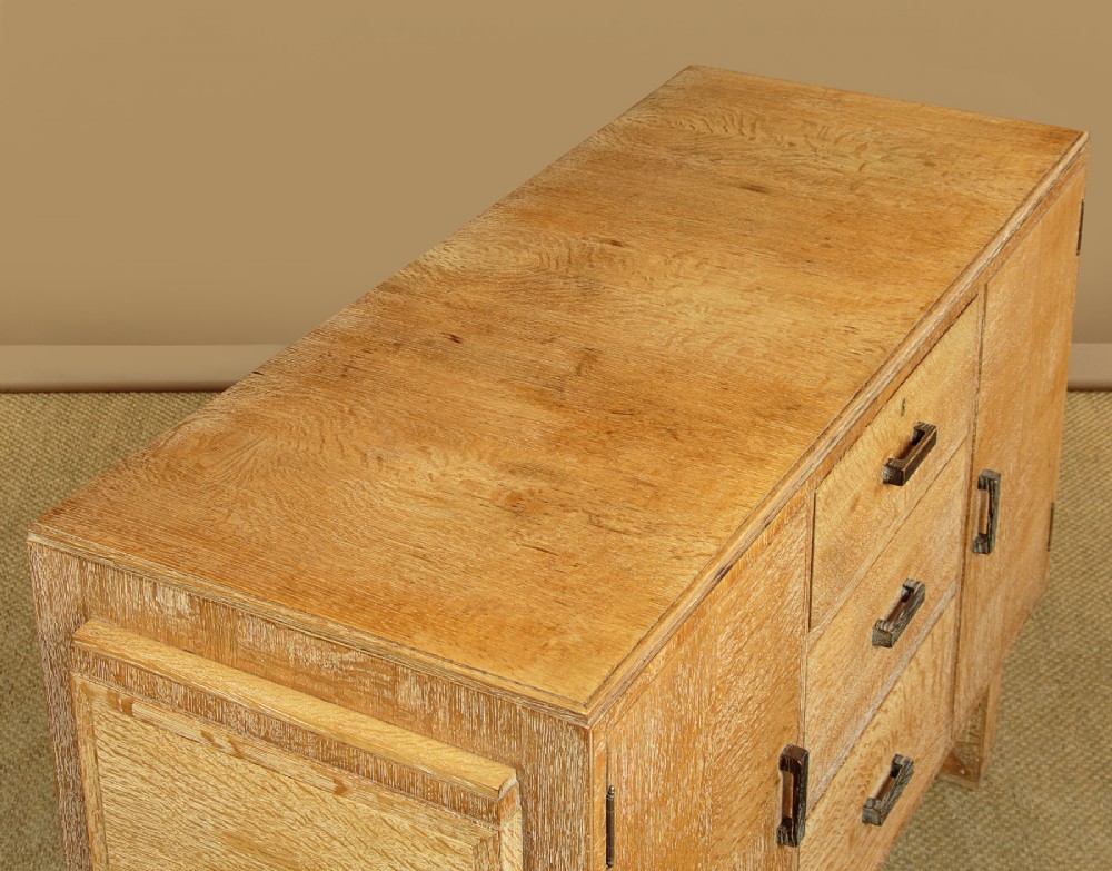 A 1920s limed oak sideboard featuring a central bank of three drawers flanked by two panelled cupboard doors on slab feet. View VI