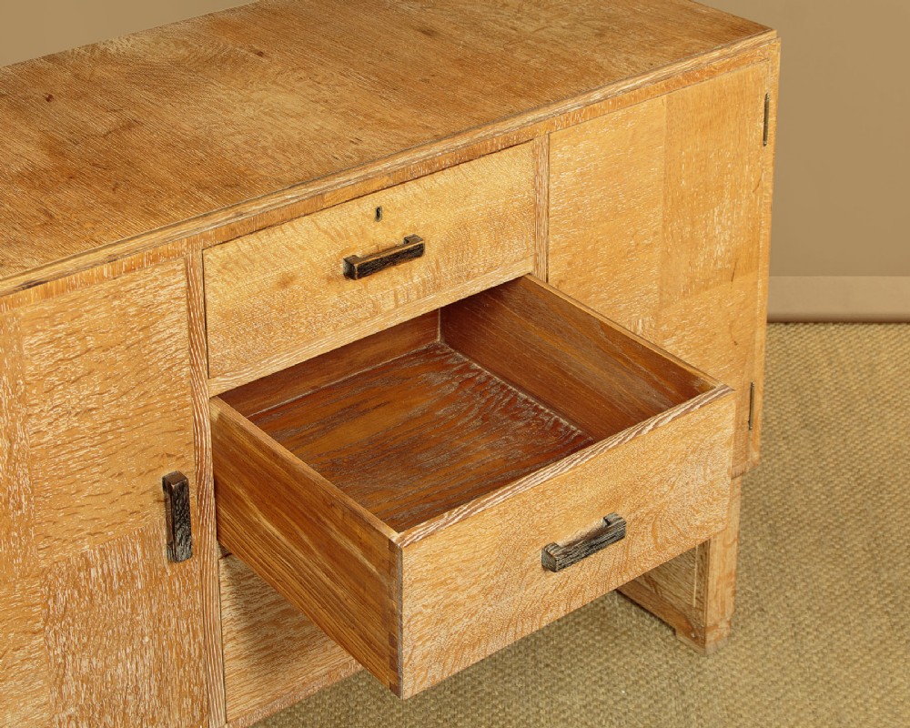 A 1920s limed oak sideboard featuring a central bank of three drawers flanked by two panelled cupboard doors on slab feet. View VIII